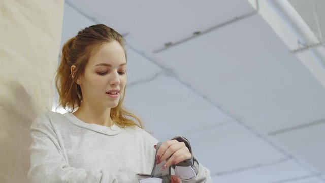 Close up of Caucasian female rollerblader sitting down in indoor rollerdrome, fixing safety pads on her hands and then continuing rollerblading