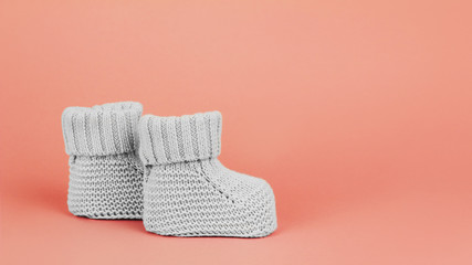 Grey baby booties on pink background, 16x9 banner, Copy space. Infant clothes and footwear concept.