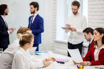 Obraz premium group of young caucasian business leaders gathered in office to discuss projects and ideas together, colleagues sit on table and have conversation. Business people concept