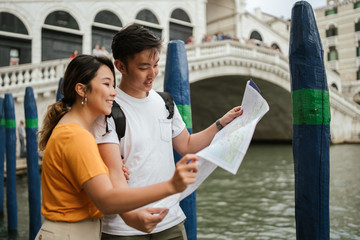 Asian couple in love looking the map of the city of Venice near the Rialto Bridge - Millennials...