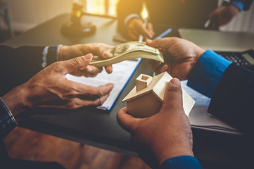 Hands with money and miniature house. Concept of real estate and deal.
