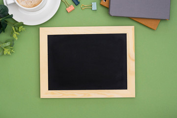 Top view of chalkboard frame with coffee cup, over green background. Mock up for design. Copy space.