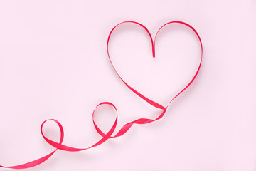 Valentines day concept red ribbon in the shape of a heart on a pink background