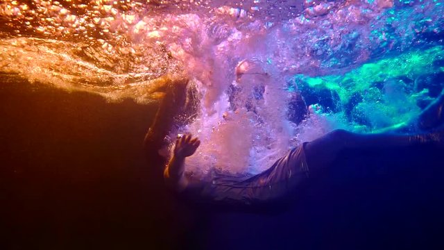 underwater shot in swimming pool, woman is falling inside water, plunging and diving