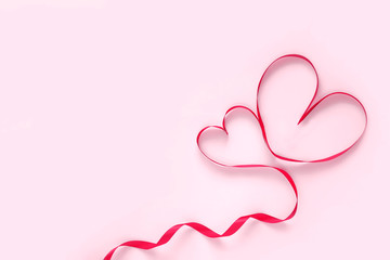 Valentine's Day concept red ribbon in the shape of 2 hearts on a pink background