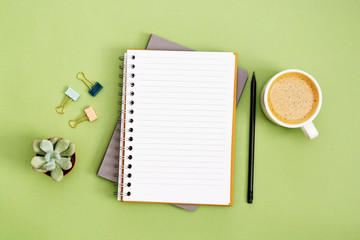 Open notebook with empty page and coffee cup. Table top, work space on green background. Creative flat lay.