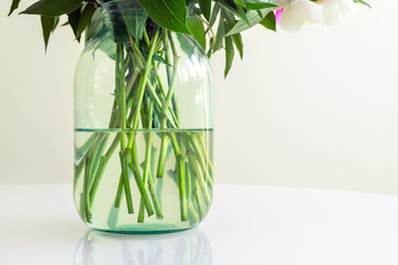 Close-up gren fresh flower bouquet stem in transparent glass jar vase with clean water on table in room indoor. Details bootom part of petal plant stalk