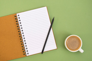 Open notebook with empty page and coffee cup. Table top, work space on green background....