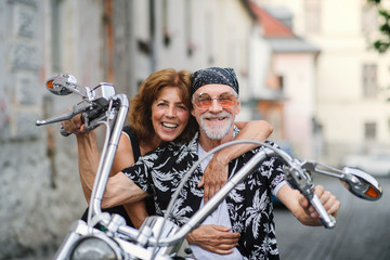 A cheerful senior couple travellers with motorbike in town.