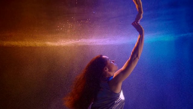 woman is floating inside pool underwater and stretching hand to surface, touching reflection
