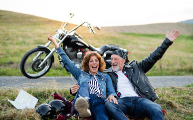 A cheerful senior couple travellers with motorbike in countryside.