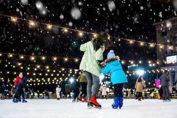 Street skating rink. Mom with daughter at the ice rink. It snows.