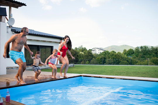 Young Family With Two Small Children By Swimming Pool Outdoors.