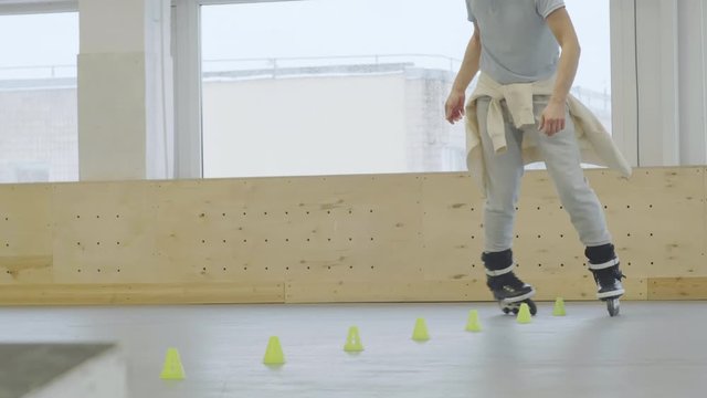 Medium shot of Caucasian male inline skater wearing professional roller-skates performing backward slaloming in indoor rolling center