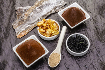 Set of traditional Japanese ingredient for cooking basic dashi broth. Algae kombu and wakame, miso paste, katsuobushi and dry granules. Black ceramic plate background