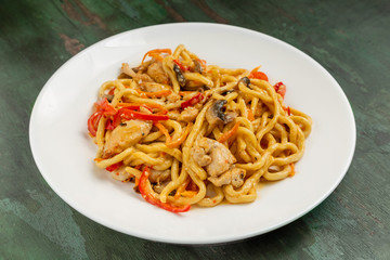 Wok noodles with meat and vegetables in a white plate on a wooden background