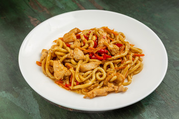 Wok noodles with meat and vegetables in a white plate on a wooden background