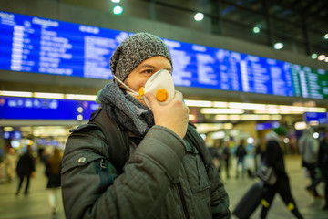 Man wearing a respirator mask device for health protection at an airport or railway train station in a crowd of people while travelling. Epidemic corona virus infection, flu sickness travel concept
