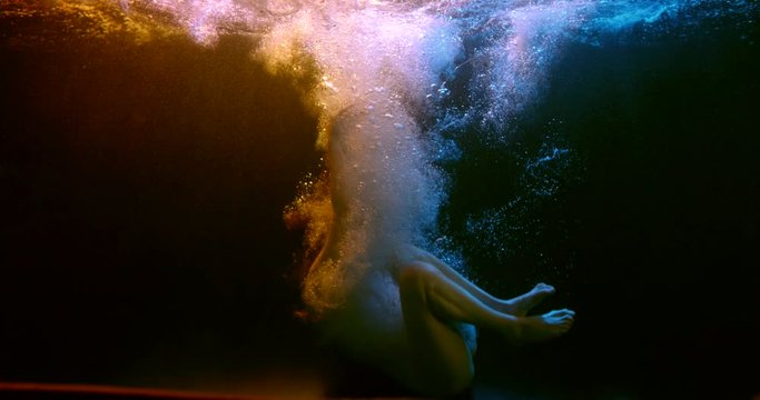 beautiful naked woman is falling on bottom of pool, underwater view, in fetal position