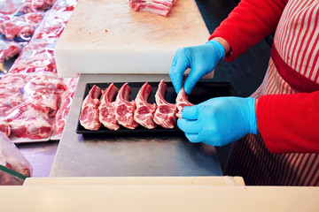 Hands of a butcher setting raw lamb ribs in a butcher shop