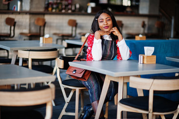 Сonfident young african american woman in smart casual wear with handbag at cafe.