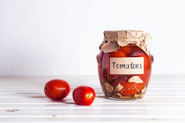Home-made pickled tomatoes in a glass jar on a light background with copy space. Horizontal orientation