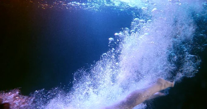 young naked woman is diving in water of swimming pool, subaquatic shot in slow motion