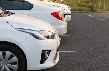 Closeup of front side of white car and other cars parking in outdoor parking lot in the evening. 