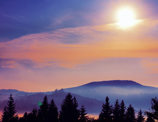 Mountain landscape in the early morning. Fantasy fabulous image. Silhouettes of mountains and fir trees on the background of a sunset dawn sky.