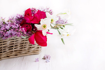 Bouquet of spring flowers in a basket on a light background, soft focus