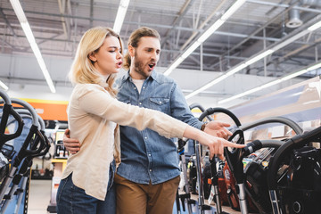 Fototapeta na wymiar shocked boyfriend and girlfriend pointing with finger at new vacuum cleaner in home appliance store