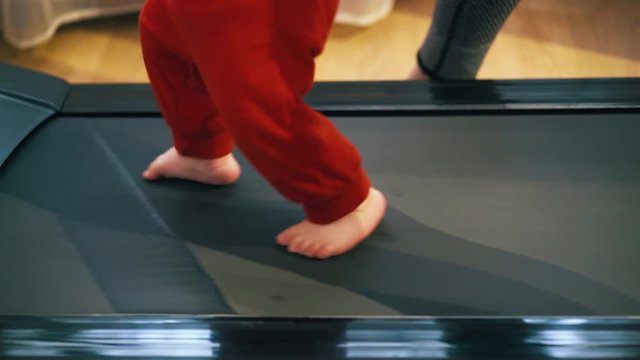 CU: funny barefoot little child in loose pants walks along modern athlete track in light room closeup