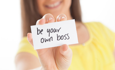 Smiling business woman holding card 'Be your own boss'