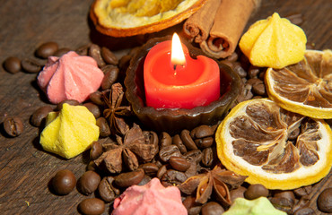 A burning candle , various spices, dried oranges and small meringues on a wooden table top.