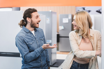 shocked boyfriend looking at smiling girlfriend in home appliance store