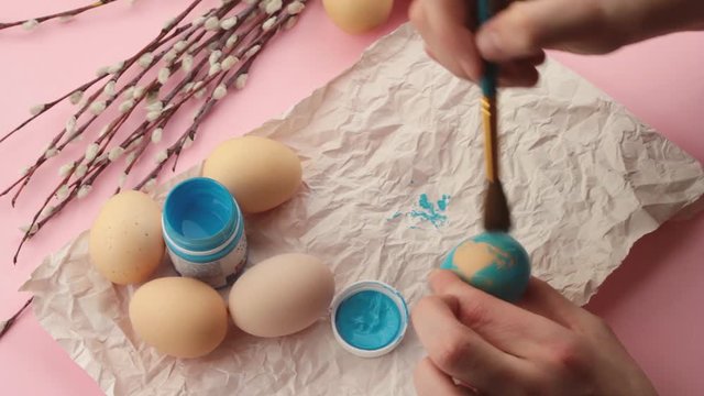 young hands paint Easter eggs on a pastel pink background. Preparing for Easter. Easter egg hunt