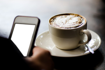 Latte coffee cup at coffee shop. Using mobile near coffee cup