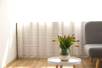Empty apartment with minimal loft style interior, wooden floor and glass vase with bouquet of tulips on foreground and blank wall with a lot of copy space for text on background. Close up.