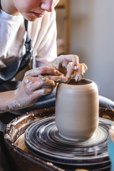 Potter working on a Potter's wheel making a vase. Woman forming the clay with her hands creating jug in a workshop.
