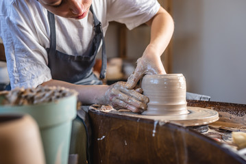 Potter working on a Potter's wheel making a vase. Young woman forming the clay with hands creating jug in a workshop.