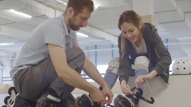 Medium shot of male inline skater helping young Caucasian woman lacing up roller-skates