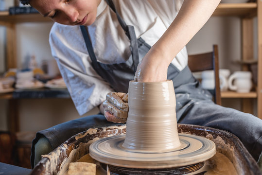 Potter working on a Potter's wheel making a vase. Young woman forming the clay with hands creating jug in a workshop.