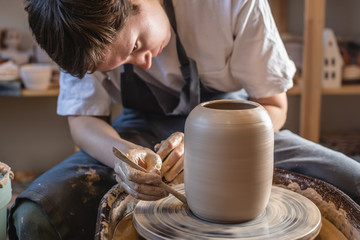 Woman potter working on Potter's wheel making a vase. Master forming the clay with her hands creating jug in a workshop