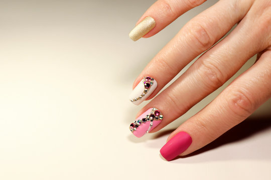 A luxurious manicure with a pink matte finish for nails and a gradient from white with gold to pink nail Polish.Nail art with various shaped rhinestones and colors.