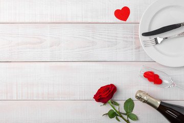 Valentines day dinner romantic festive setting, red tape, kraft gift box, champagne wine glass, bottle, roses, hearts, silverware on white wooden background. Copy space, place for text. Top view.