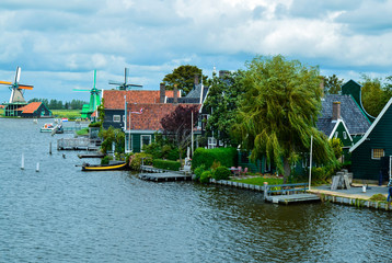 Fototapeta na wymiar Zaanse Schans, Holland, August 2019. Northeast Amsterdam is a small community located on the Zaan River. View of the mills on the river bank, they stand out with their bright colors. Cloudy day.