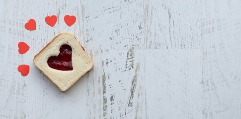 Toast with heart-shaped jam on a pink plate, wooden white table flat lay