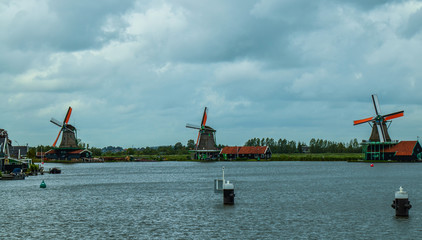 Fototapeta premium Zaanse Schans, Holland, August 2019. Northeast Amsterdam is a small community located on the Zaan River. View of the mills on the river bank, they stand out with their bright colors. Cloudy day.