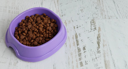 Fototapeta na wymiar Dry cat food in purple plate on a white table, space for text