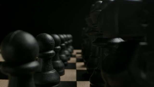 Black chess figures in start position ready to game concept. Wide macro shot sliding between two rows of chess figures and pawns.